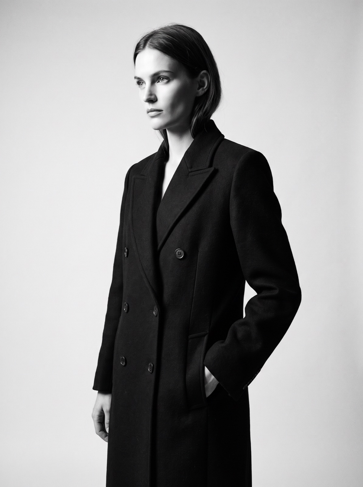 Black-and-white editorial photograph of a model in a tailored wool overcoat