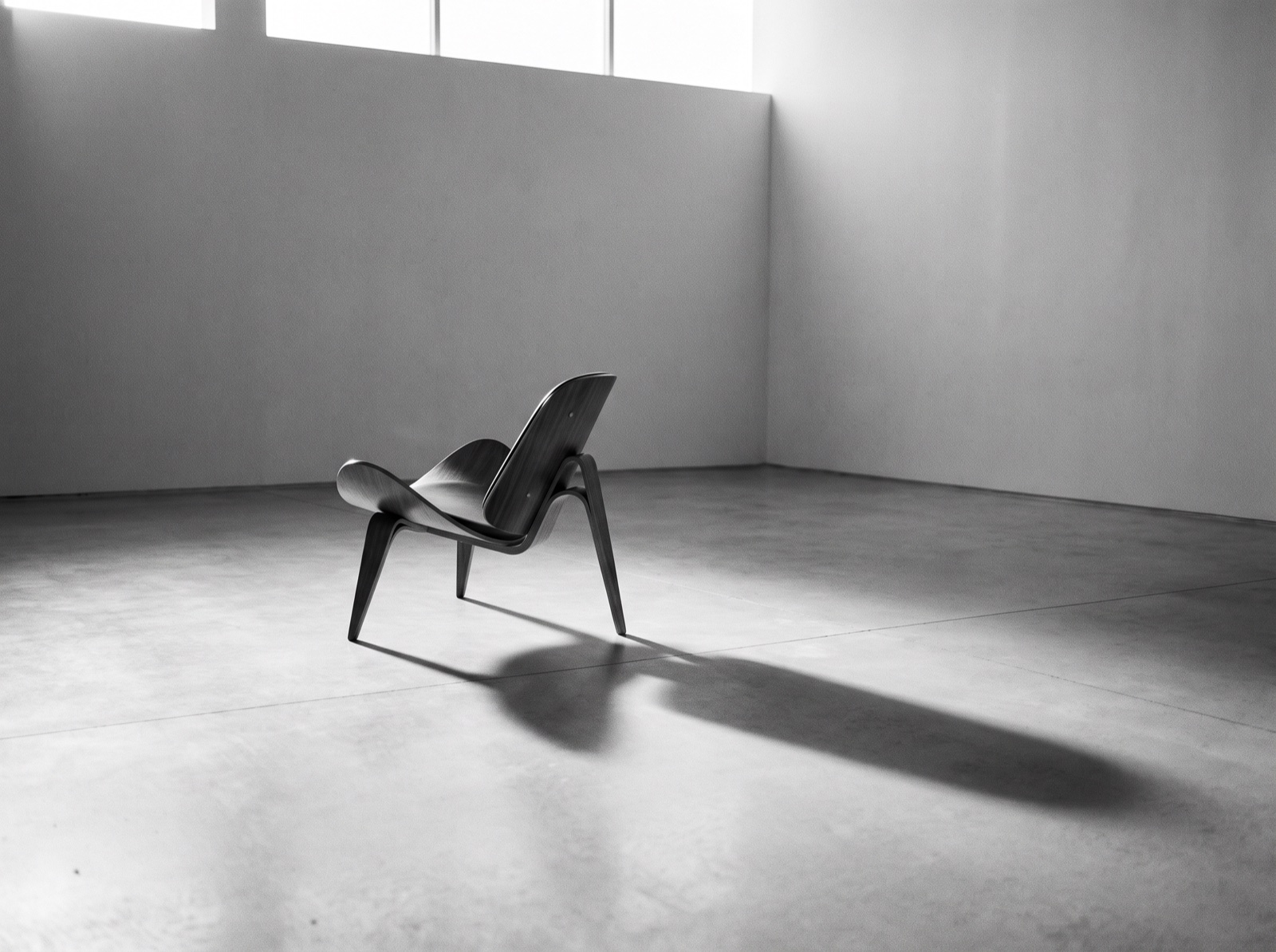 Black-and-white photograph of a sculptural lounge chair casting a long shadow in an empty gallery
