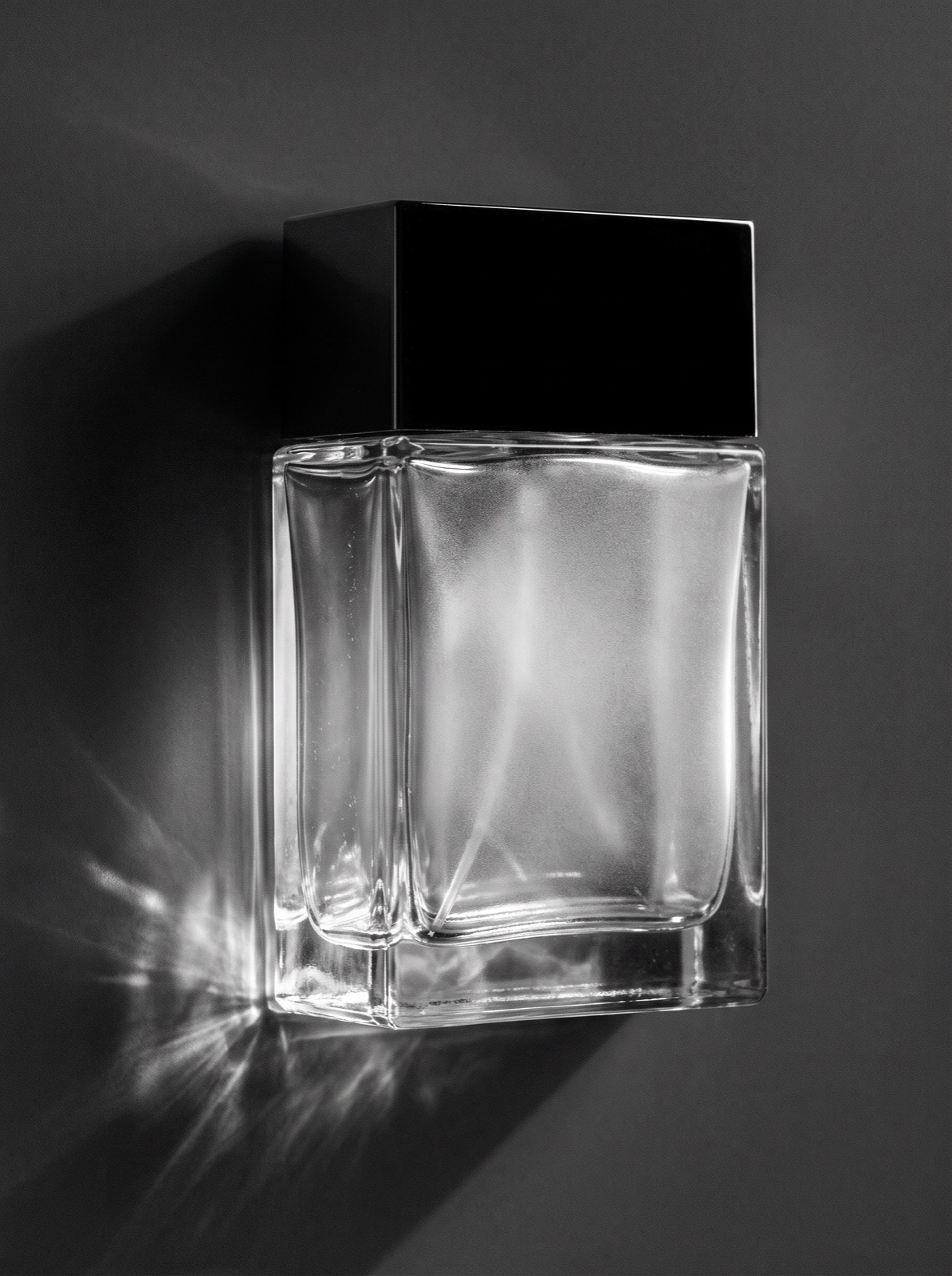 Black-and-white macro photograph of an unlabeled glass perfume bottle in dramatic side light