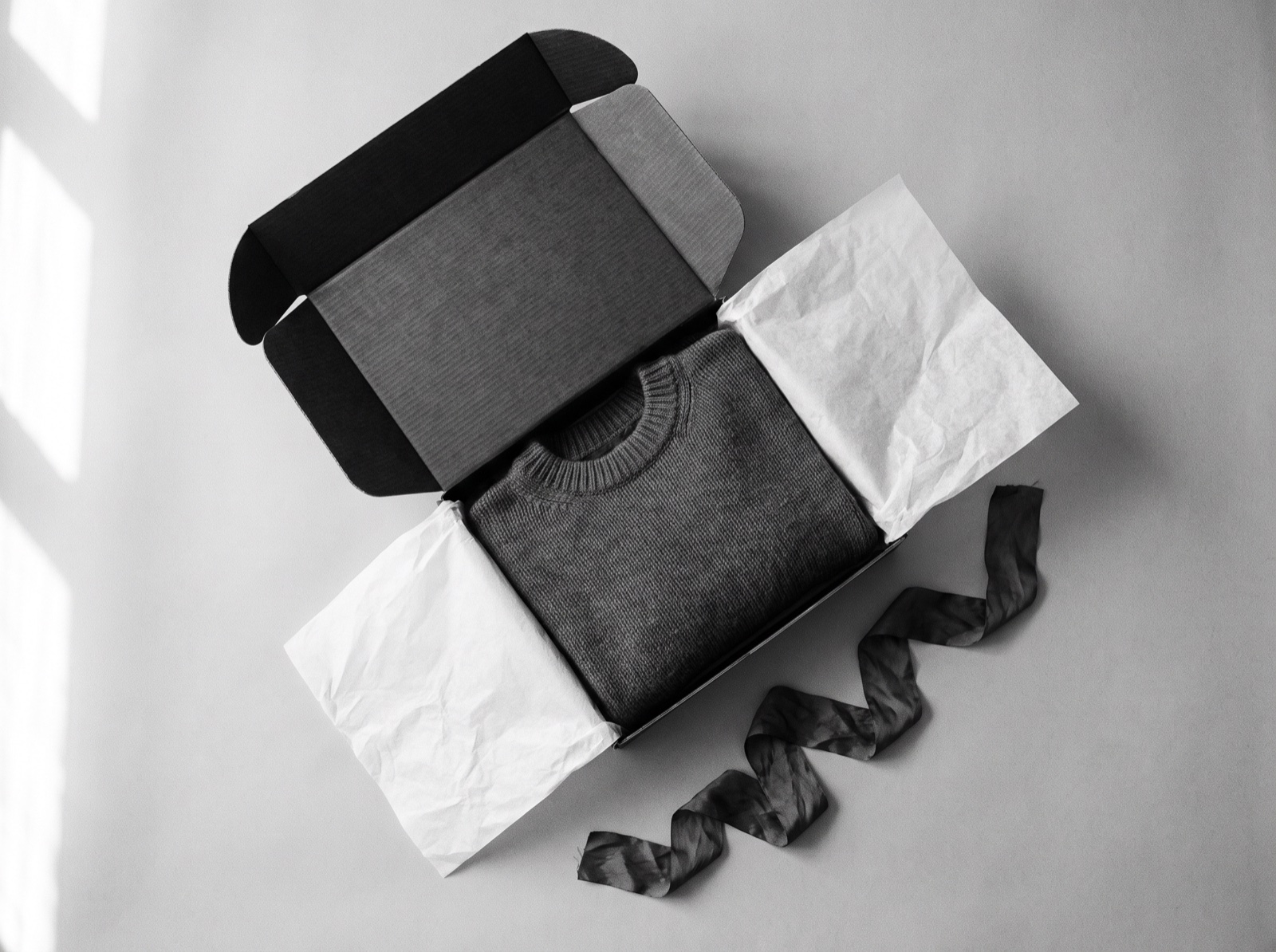 Black-and-white overhead photograph of an opened premium box with tissue paper and a folded garment